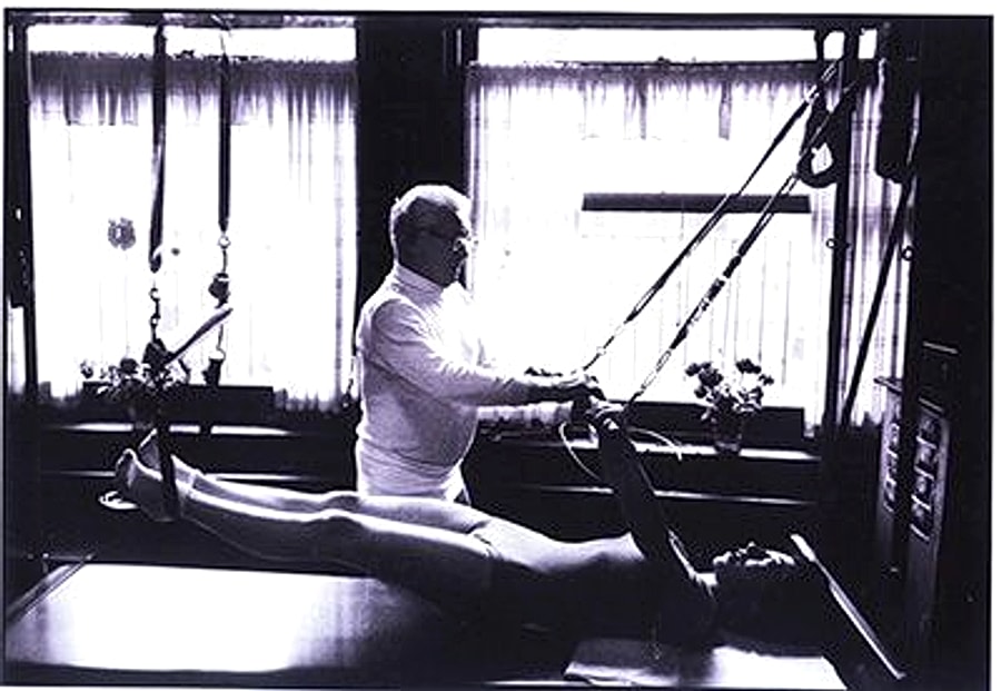 Joseph Pilates orientando um exercício no Reformer em seu studio