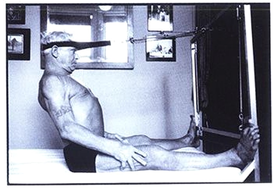 Joseph Pilates praticando um exercício sentado no Reformer
